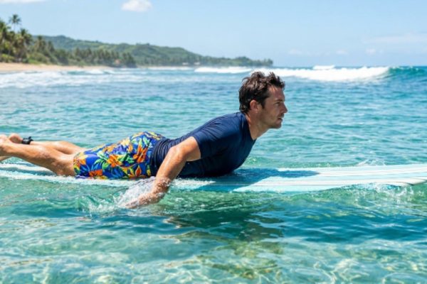 A man wearing colorful men's boardshorts paddling out on a surfboard in clear blue ocean water