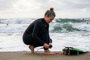 Surfer attaching a surfboard leash to their ankle before paddling out into ocean waves