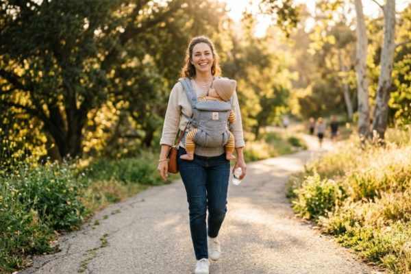 A happy mother wearing a comfortable ergonomic baby carrier outdoors in California.
