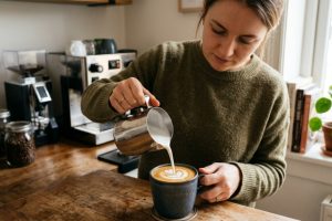 Handheld milk frother whipping foam in a ceramic coffee mug.